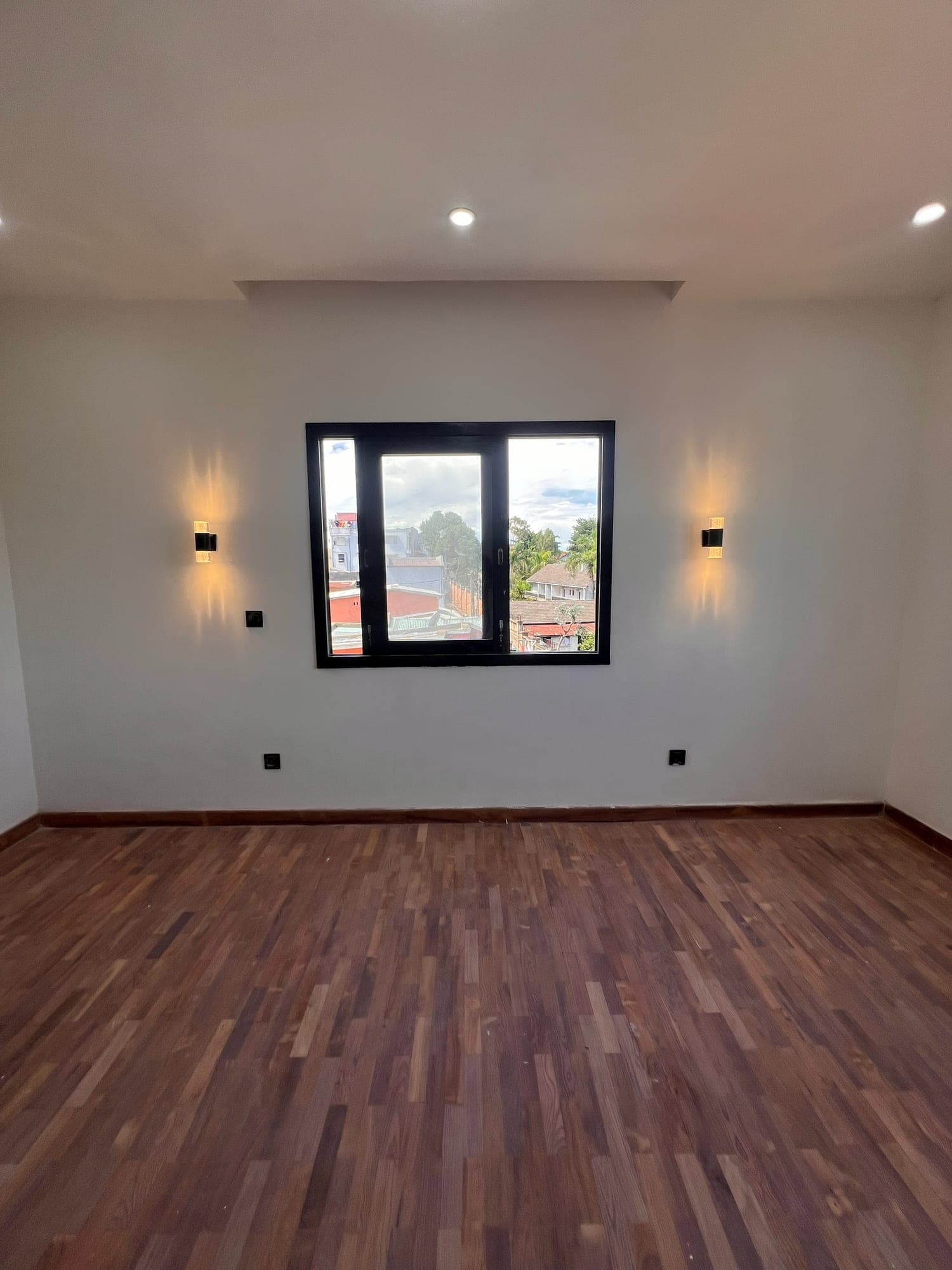 Pièce au parquet massif, fenêtre ouverte sur Antananarivo