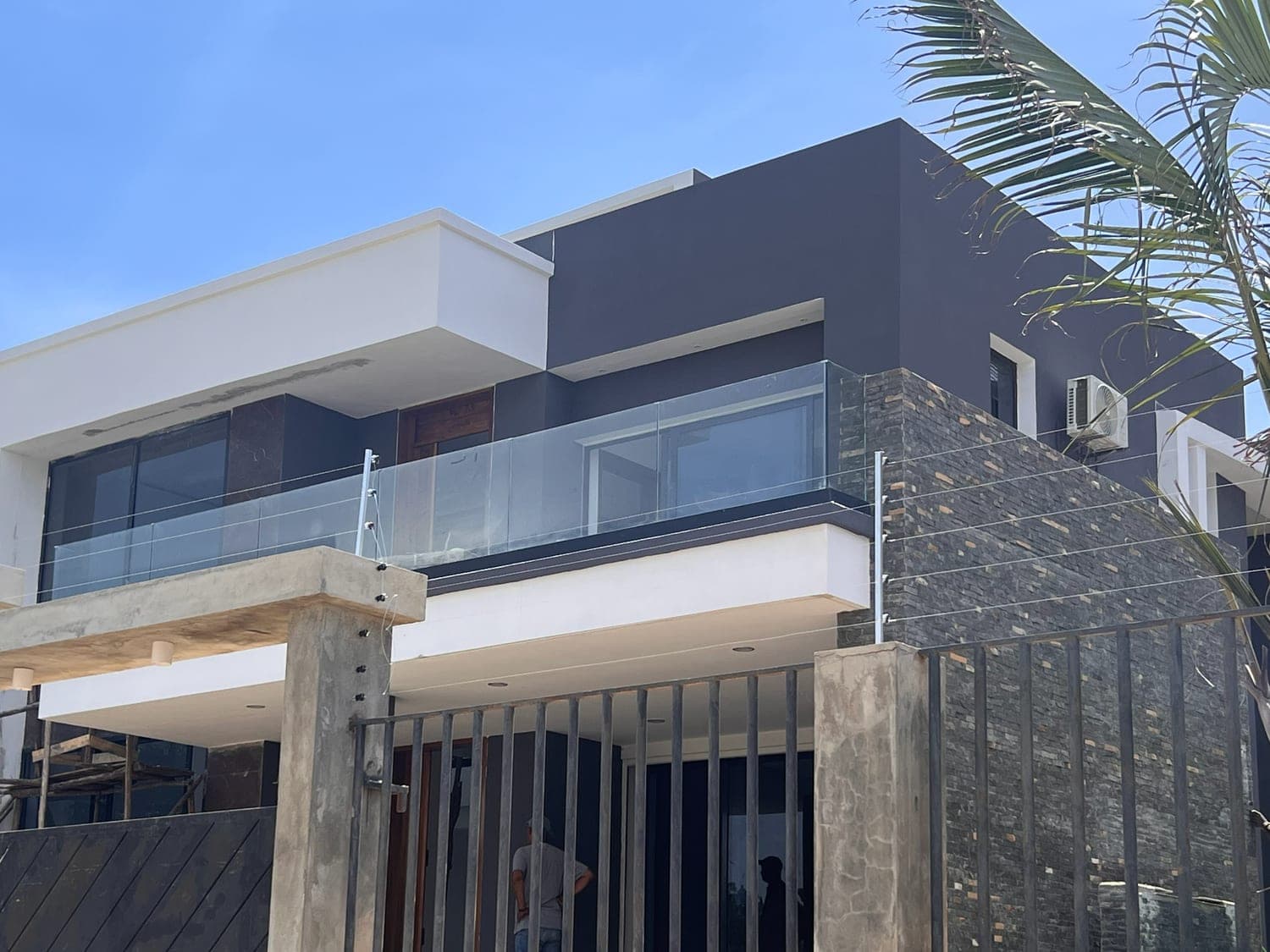 La même villa construite : étage, parement de pierre, garde-corps en verre et palmier