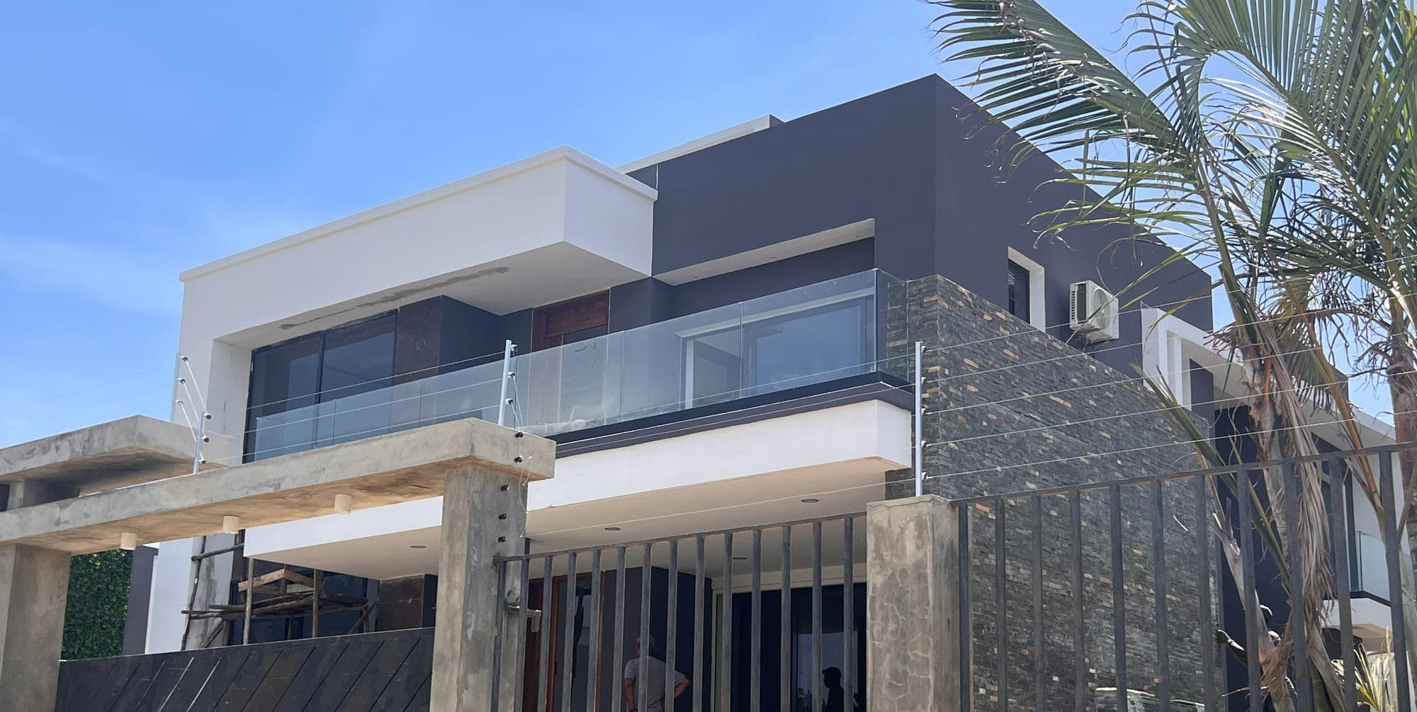 La même villa construite : étage, parement de pierre, garde-corps en verre et palmier
